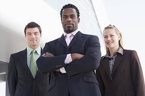 Three businesspeople standing outdoors by building smiling