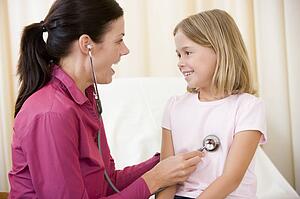 Doctor giving checkup with stethoscope to young girl in exam room smiling