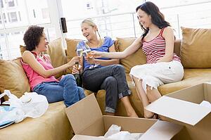 Three girl friends toasting champagne by boxes in new home smiling