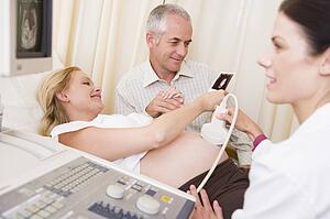 Pregnant woman getting ultrasound from doctor with husband looking at picture