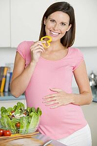 Pregnant woman in kitchen making a salad and smiling