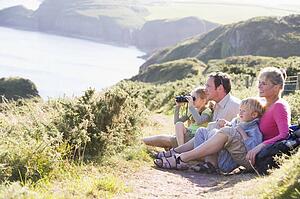 Family on cliffside path using binoculars and smiling
