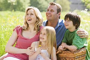Family sitting outdoors with picnic basket smiling