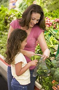 Mother and daughter shopping for broccoli at a grocery store