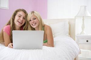 Teenage Girls Lying On Bed Using Laptop