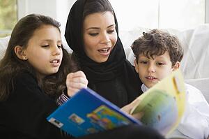 Mother and two young children in living room reading book (high key/selective focus)