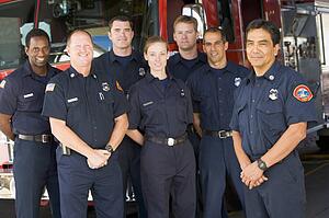 Six firefighters standing in front of fire engine with captain (depth of field)