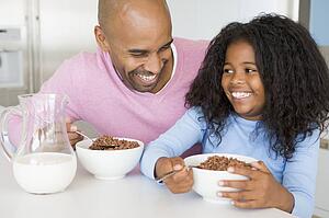 Father Sitting With Daughter As She They Eat Breakfast