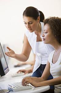 Two women in computer room where one is assisting the other