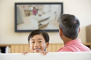 Man and young boy in living room with flat screen television smiling