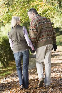 Couple outdoors walking on path in park holding hands and smiling (selective focus)