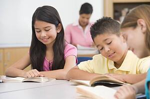 Students in class reading with teacher in background (selective focus)