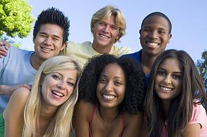 Six people outdoors huddling over camera