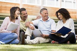 Adult students on lawn of school studying and talking