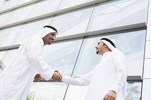 Two businessmen outdoors by building shaking hands and smiling