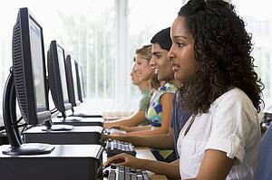 Four people sitting at computer terminals (depth of field/high key)