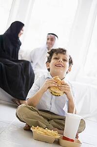 Young boy with fast food in living room laughing with parents in background (high key/selective focus)