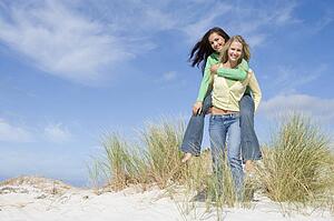 Young woman giving piggyback ride to her friend on a sand hill