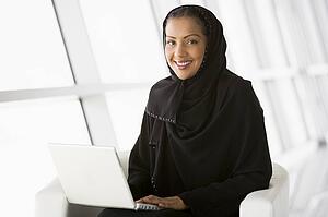 Woman sitting indoors with laptop smiling (high key/selective focus)