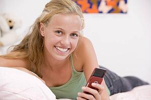 Teenage Girl Lying On Her Bed Using Mobile Phone