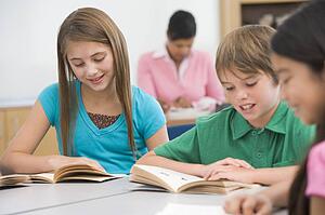 Students in class reading with teacher in background (selective focus)