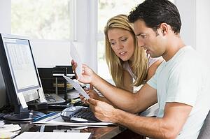 Couple in home office with computer and paperwork looking unhappy