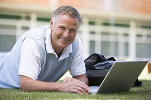 Man lying on lawn of school with laptop