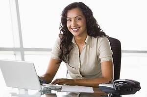 Businesswoman in office with laptop smiling (high key/selective focus)