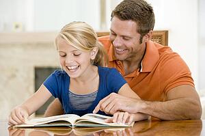 Man and young girl reading book in dining room smiling