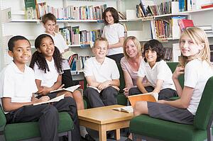Seven students in library reading books with teacher