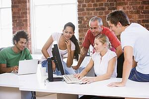Five businesspeople in office space looking at computer and smiling