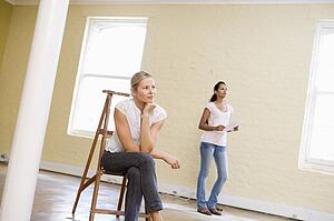 Two women with ladder in empty space holding paper