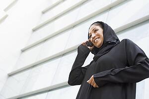 Businesswoman outdoors by building using cellular phone and smiling (selective focus)