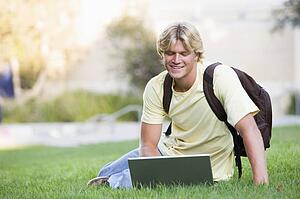 Man outdoors sitting on grass with laptop (selective focus)