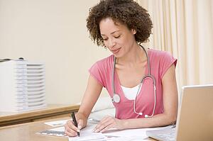 Doctor with laptop writing in doctor's office