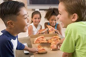 Four young children indoors eating pizza smiling
