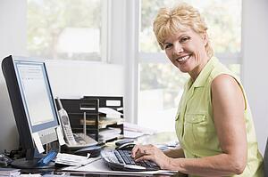 Woman in home office at computer smiling