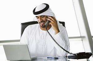 Businessman in office with laptop on telephone smiling (high key/selective focus)