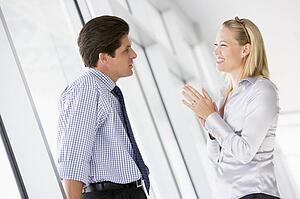 Businessman standing in corridor talking to smiling businesswoman