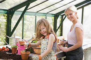 Young girl and woman in greenhouse putting soil in pots smiling