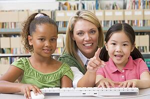 Two students in class at computer keyboard with teacher
