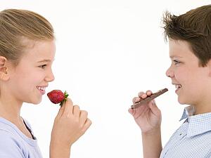 Sister eating strawberry by brother eating chocolate bar