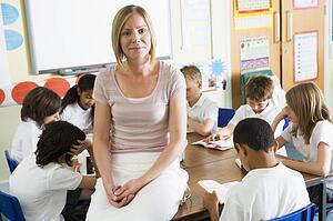 Students in class reading books with teacher in foreground