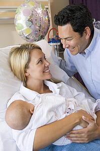 New mother with baby and husband in hospital smiling