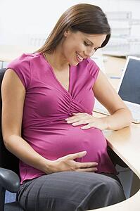 Pregnant woman at work holding belly and smiling