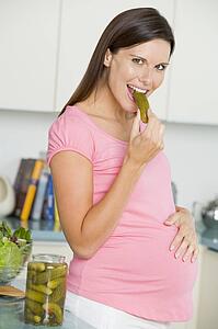 Pregnant woman in kitchen eating pickles and smiling
