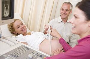 Pregnant woman getting ultrasound from doctor with husband watching