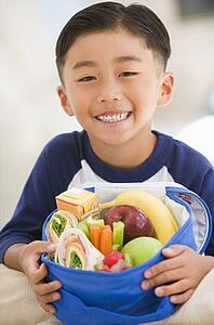 Young boy indoors with packed lunch smiling