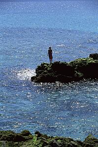 Woman outdoors standing on large rocks Oceanside (far away)
