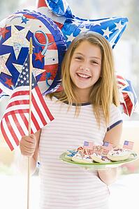 Young girl outdoors on fourth of July with flag and cookies smiling